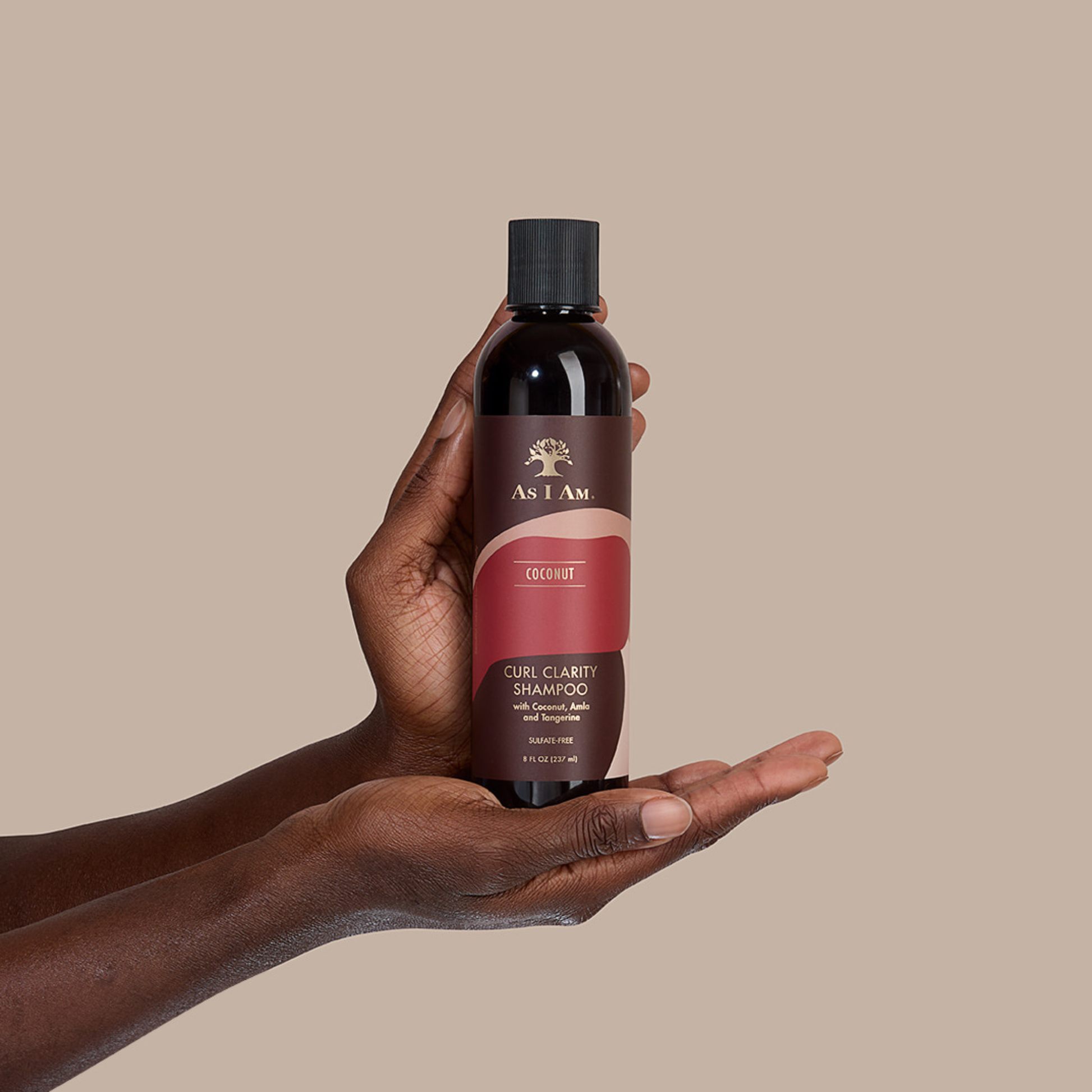 يد تحمل زجاجة من شامبو As I Am Coconut Curl Clarity على خلفية بيج