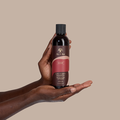 يد تحمل زجاجة من شامبو As I Am Coconut Curl Clarity على خلفية بيج