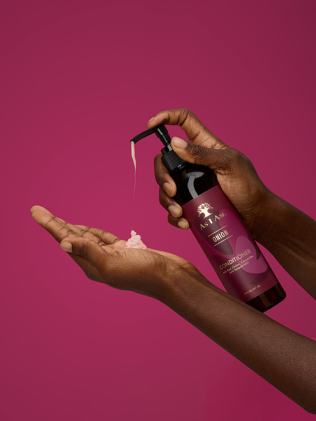 يد تحمل زجاجة من بلسم as i am مع المنتج على راحة اليد على خلفية وردية