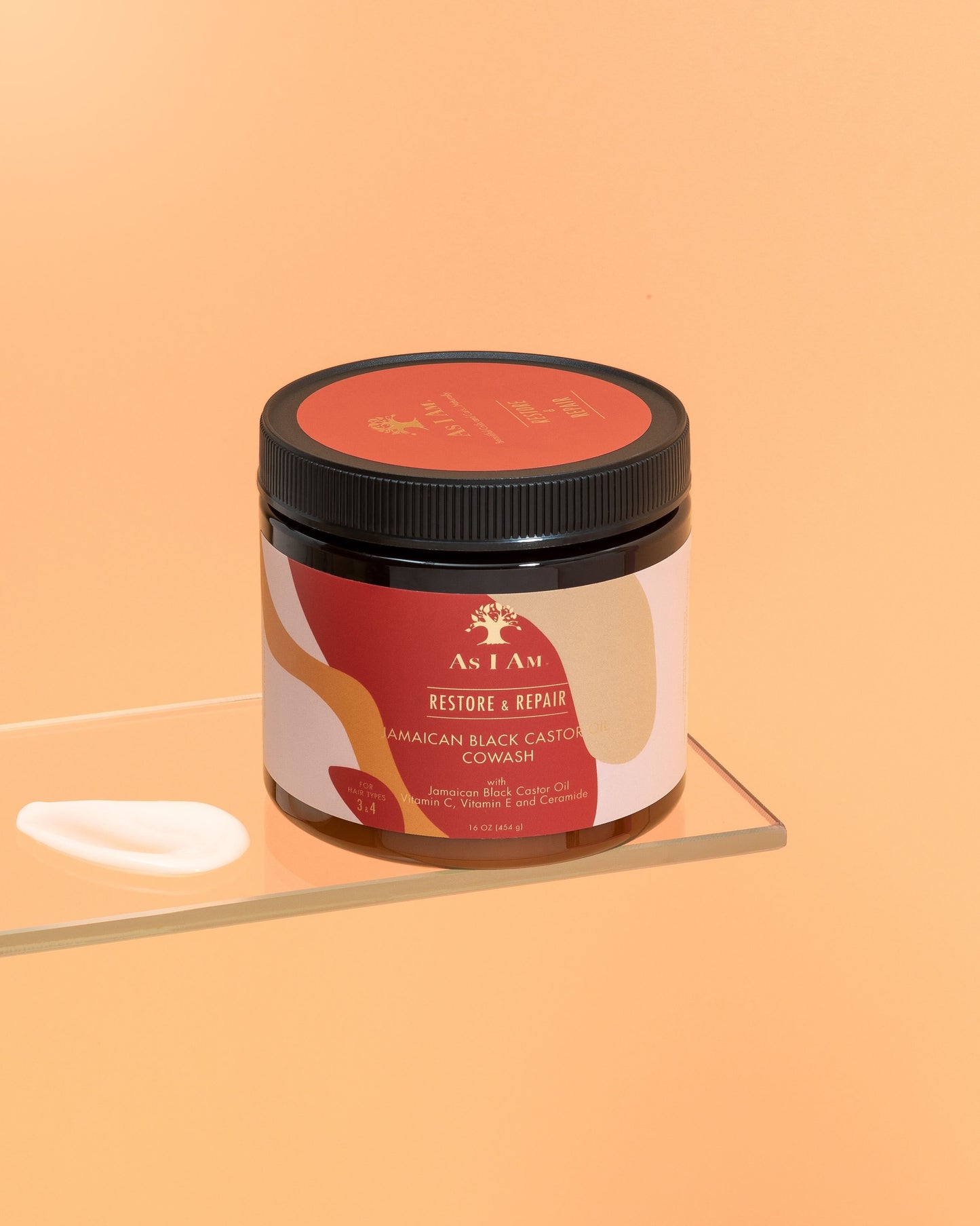 عبوة من زيت الخروع الأسود الجامايكي Cowash مع ملصق يوضح تفاصيل المنتج، موضوعة على سطح عاكس بخلفية برتقالية صلبة.