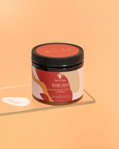 عبوة من زيت الخروع الأسود الجامايكي Cowash مع ملصق يوضح تفاصيل المنتج، موضوعة على سطح عاكس بخلفية برتقالية صلبة.